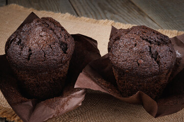 Two chocolate muffins in a paper cup on a burlap napkin.