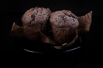 Two chocolate muffins in a paper cup on a dark background.