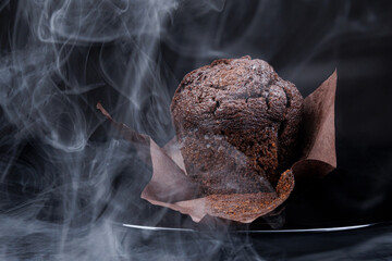 Chocolate muffin in an unfolded paper cup on a dark background. Steam comes out of the hot chocolate muffin.
