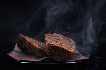 Sliced chocolate muffin in a black plate on a dark background. Steam comes out of a fresh chocolate muffin.