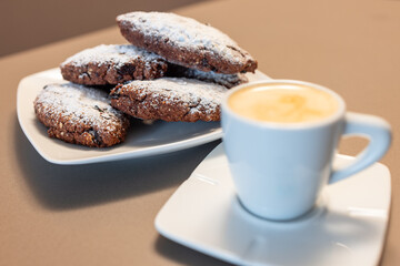 Pan dei Morti cookies with powdered sugar and a cup of caffe macchiato in soft focus, showcasing a classic Italian coffee pairing