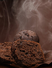 Cut chocolate muffin and whole muffin on brown background. Steam comes out from fresh chocolate muffin.