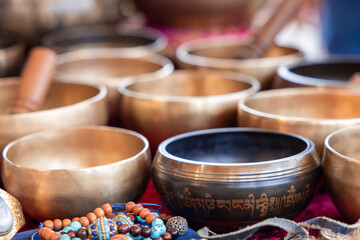Polished brass Tibetan singing bowls featuring decorative inscriptions, with vibrant beaded jewelry and meditation tools arranged nearby