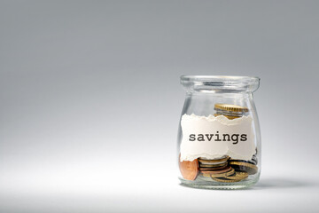 A clear glass jar contains various coins used for saving money. The jar is prominently labeled...