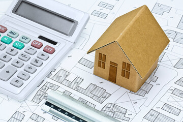 Imaginary cadastral map of territory with buildings and land parcel - concept with a small cardboard house, calculator and ruler