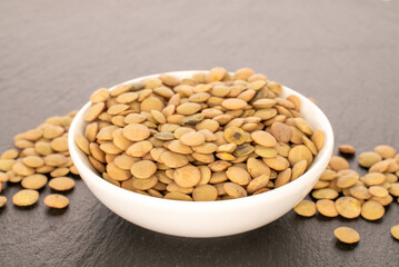 Raw lentils in a white ceramic saucer on a slate stone, macro.
