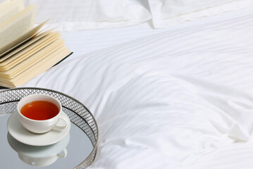 Tea, book and floral decor on bed with clean linens indoors, space for text
