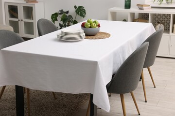 Table with white tablecloth, apples, plates and chairs in stylish room