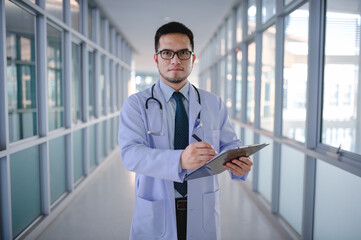 A male doctor is standing checking a list of patients in a hospital corridor.