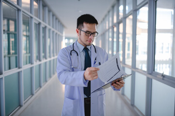 Fototapeta premium A male doctor is standing checking a list of patients in a hospital corridor.
