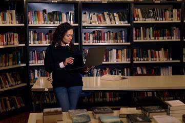 Focused woman using a laptop in a library surrounded by bookshelves