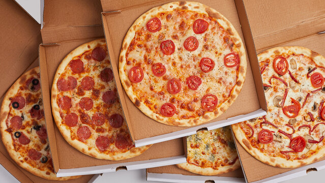 close-up cardboard boxes stand one top of the other opens with whole pizzas with different flavors pepperoni jalapeno Dorblu cheese four cheeses pizza for a large company