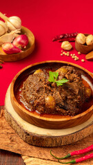 Indonesian beef rendang, Rich beef curry presents a flavorful dish garnished with fresh herbs, amidst an array of spices and aromatic ingredients nearby