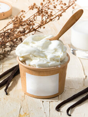 Delicious and creamy vanilla ice cream is served in a cardboard cup with a wooden spoon, accompanied by vanilla pods and dried flowers