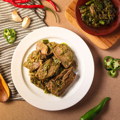 Indonesian green chili beef tongue, Slices of tender beef stewed with green peppers and spices are arranged on a white plate, surrounded by fresh chilies and garlic
