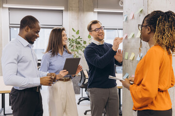 Diverse business team collaborating on a project, using sticky notes on a wall in a modern office environment