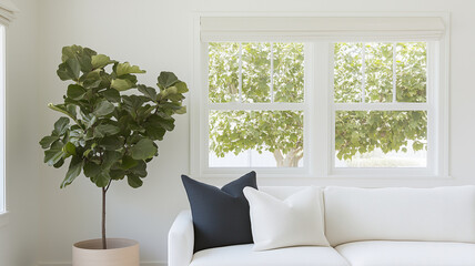 bright and airy living room featuring white sofa adorned with decorative pillows, complemented by potted plant and large windows showcasing greenery outside