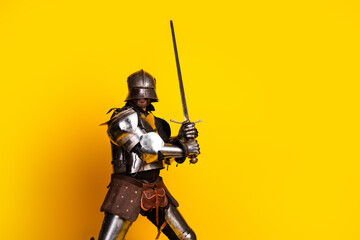 Knight in medieval armor posing with a sword against a bold yellow background