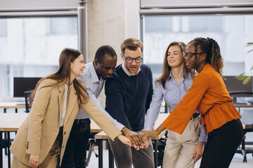 Diverse businesspeople joining hands in office, symbolizing teamwork, collaboration, and unity in...