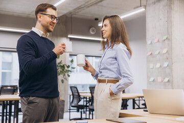 Colleagues conversing, holding coffee mugs near workspace with contemporary design