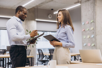 Two business colleagues discussing work together in modern office using clipboard and tablet
