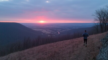 Runner enjoying a sunset view from a mountain trail overlooking a serene valley landscape