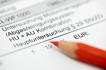 Ein Rotstift liegt auf der Rechnung zur TÜV-Hauptuntersuchung und Abgasmessung - Symbolbild