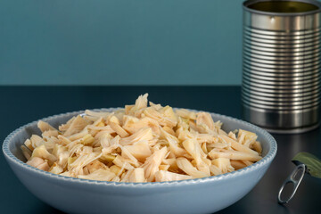 Canned shredded jackfruit in a bowl, vegan substitution for chicken. Empty open can. Blue background with space for text.
