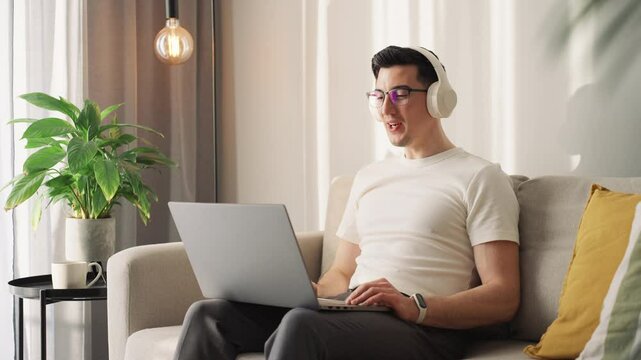 Morning hustle, but make it cozy. A businessman lounges on a sofa, laptop open, headphones on, waving into a virtual meeting. Sunlight streams in, casting a warm glow over the Mocha Mousse tones