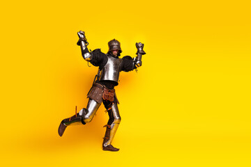 Energetic knight in medieval armor jumping against a vibrant yellow backdrop