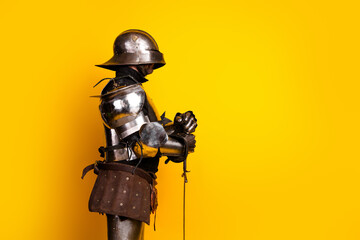 Side view of an armored knight in full metallic gear holding a sword against a vibrant yellow...
