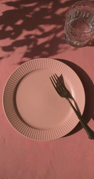 Vertical video of empty plate with fork on the mediterranean pink terracotta color plaster background with leaves shadows. Copy space