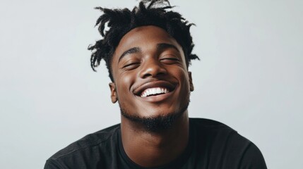Fototapeta premium Smiling young Afro man with short curly hair wearing a black shirt in a relaxed pose against a light gray studio background.