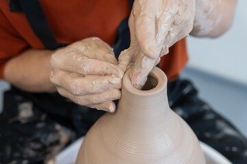 Close-up of a potter's hands making a ceramic vase on a potter's wheel. 