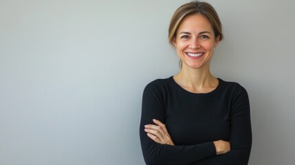 Fototapeta premium smiling woman in black long-sleeve top with arms crossed standing against light gray background expressing confidence and happiness
