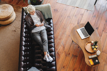 Top view of happy old mature retired woman listening popular music in headphones, relaxing alone on...