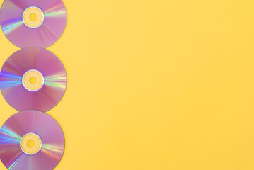 Obraz premium Line of three purple cds on yellow background with copy space