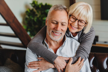 Lovely mature husband and wife sit rest on couch at home embracing and cuddling, show care affection, smiling senior loving couple relax on sofa, enjoy tender romantic family weekend moment together