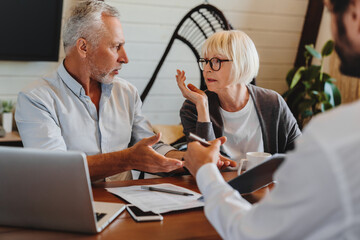 Dishonest contractor. Angry elderly couple sit at broker manager office demand compensation for breach of contract bad service. Annoyed mature spouses scam victims complain lawyer on commercial fraud