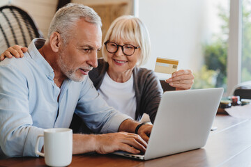 Fototapeta premium Senior couple happy laptop online shopping debit credit card order ecommerce. Portrait of happy smiling senior couple using laptop and credit card at home.