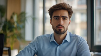 Obraz premium Young man with contemplative expression in modern office setting, wearing light blue shirt, reflecting on personal loss and emotional challenges.