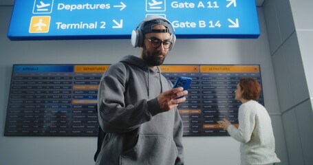 Busy Airport Terminal: Man with Backpack Checks Flight Information on Mobile Phone, Looks at...