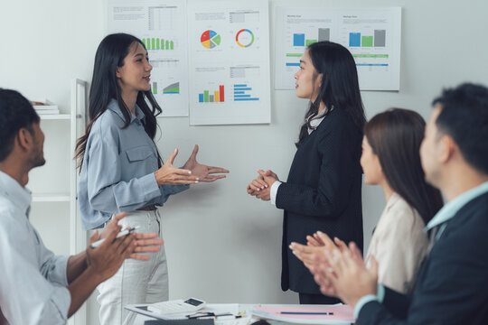 Successful Presentation: A dynamic business team applauds a confident female presenter delivering a compelling presentation, showcasing data visualizations on a whiteboard.