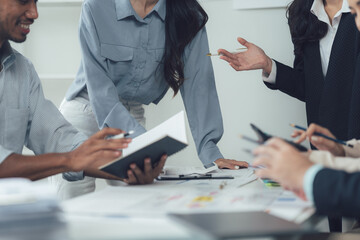 Collaborative Brainstorming: A diverse group of business professionals engage in a dynamic discussion, reviewing documents and sharing ideas in a modern office setting.