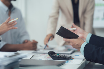 Business Meeting Close-up: Hands holding a notepad, surrounded by colleagues in a focused business...
