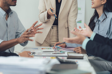Strategic Business Meeting: A diverse team of business professionals engages in a lively discussion around a table filled with charts and reports, showcasing collaboration and strategic planning.