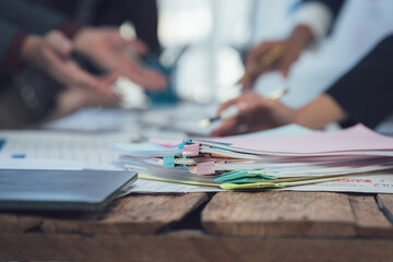 Focused Teamwork: A close-up shot showing a stack of documents and papers on a rustic wooden table,...