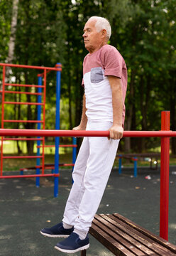Elderly sportive man doing parallel bars exercise in park