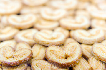 A close up of many small, round, golden brown cookies with a heart shape. The cookies are piled on top of each other, creating a visually appealing and appetizing display