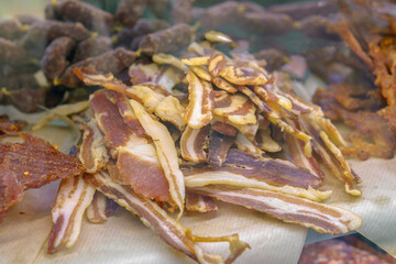 A pile of bacon strips on a table. The bacon is cut into strips and is spread out on a piece of paper